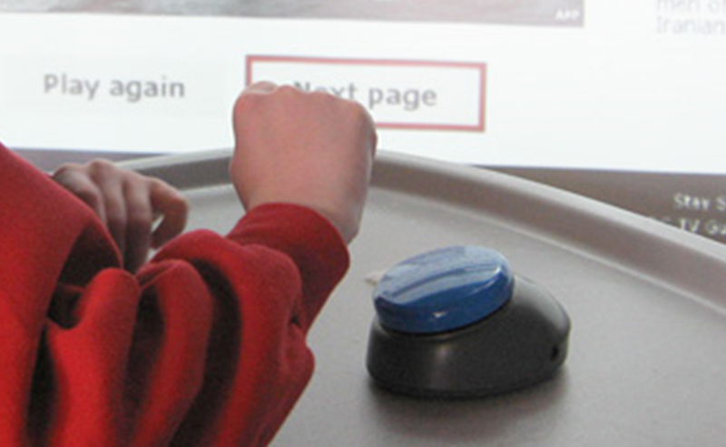 Child operating a computer by using a single large button mounted on a tray in front of her